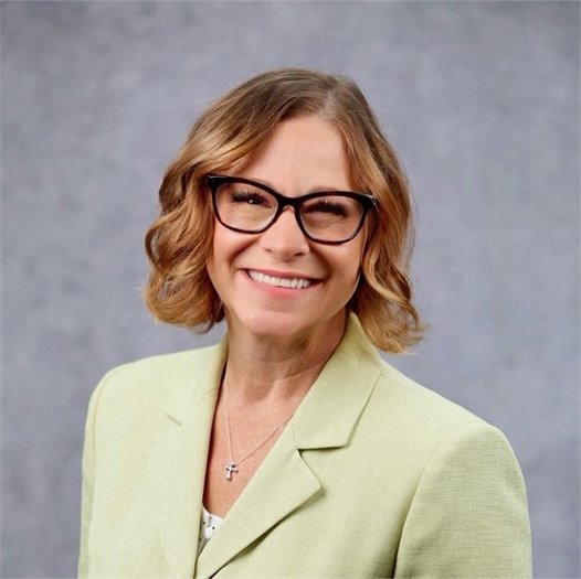 A picture of April Mitts. She is wearing a light green suit jacket, against a gray background